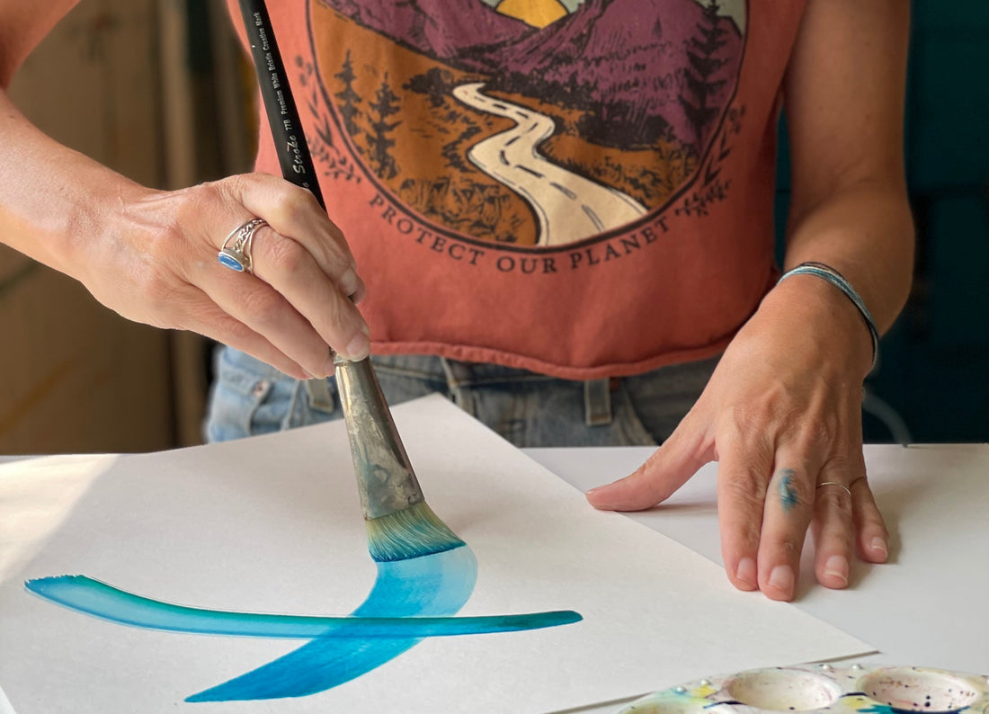 Artist Sunni Mocking bird working in studio with blue watercolor and large paintbrush